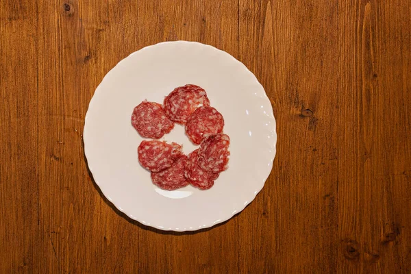 Top view of plate with salami slices on wooden background — Stock Photo, Image