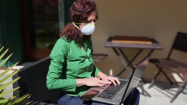 Mujer sentada en el jardín, usando una máscara anti-covidio, mientras usa su computadora portátil — Vídeo de stock