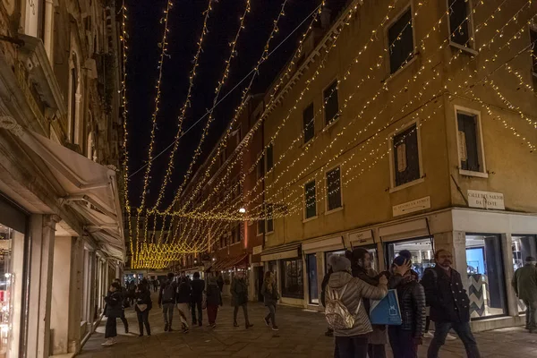 Turistas en calle veneciana por las noches con boutiques y decoraciones navideñas — Foto de Stock