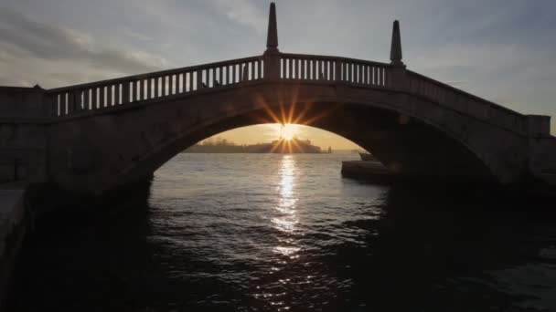 Glimpse under the vault of a bridge of the sun rays at sunset behind a church — Stock Video
