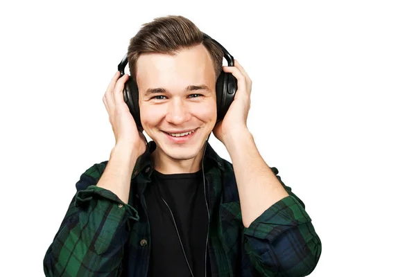 Porträtt av en kaukasiska vit ung kille lyssna musik i örat-telefoner. Stilig man klädd i en svart T-shirt och en grön rutig skjorta på vit isolerade bakgrund — Stockfoto