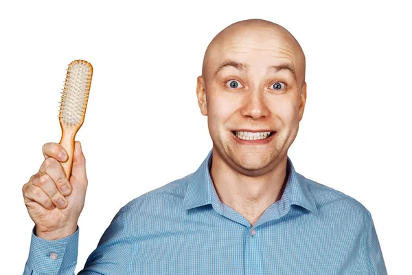 Portrait of a bald guy in a blue shirt holding a comb in his hands on an isolated white background. The concept of hair loss and hair transplantation