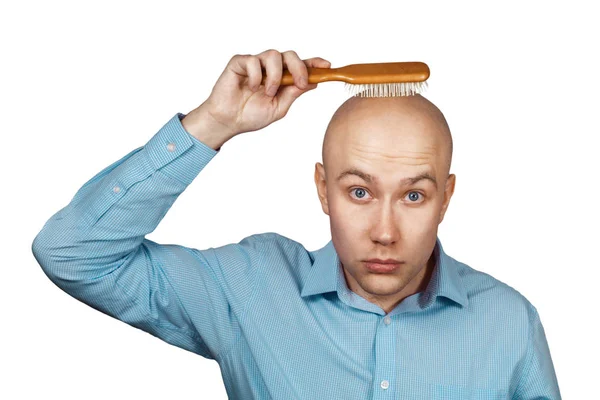 Portrait of a bald guy in a blue shirt holding a comb in his hands on an isolated white background. The concept of hair loss and hair transplantation — Stock Photo, Image