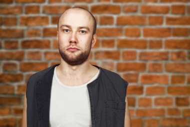 Kolsuz gömlek giymiş pocker yüzü ile sakal ile portre genç kel adam. Tuğla üzerinde adam. duvar arka plan.