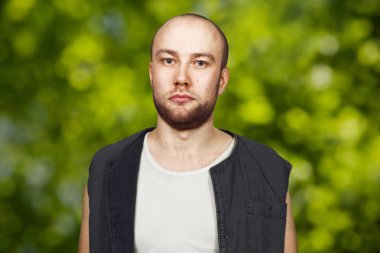 Kolsuz gömlek giymiş pocker yüzü ile sakal ile portre genç kel adam. Yeşil bokeh arka planda adam.