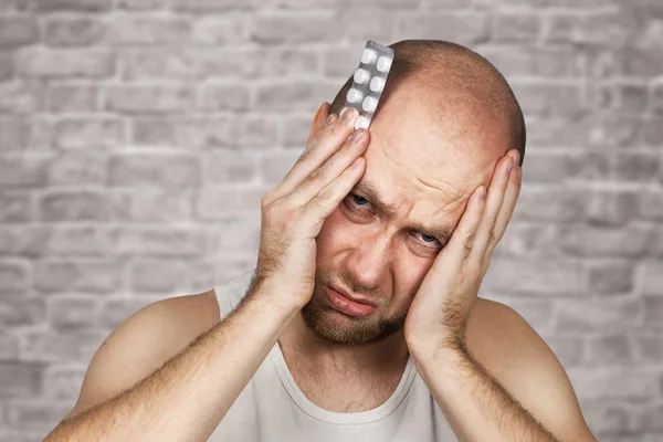 Hombre tomando antibiótico, antidepresivo, medicación de la píldora para aliviar dolor en el hogar. Joven enfermo, enfermo que sufre de dolor de cabeza, estrés o gripe, concepto de tratamiento de emergencia en el fondo de la pared de ladrillo — Foto de Stock