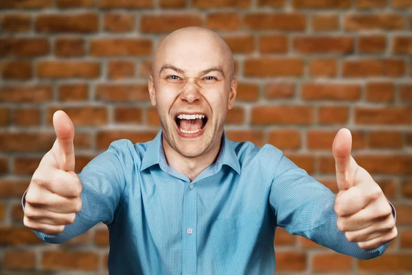 Retrato Hombre calvo blanco en camisa azul sobre fondo de pared de ladrillo mostrando pulgares hacia arriba y sonriendo — Foto de Stock