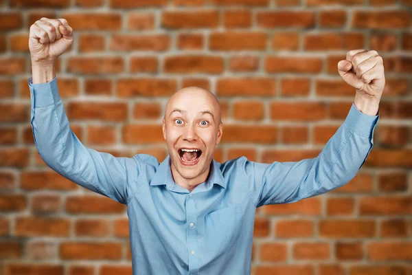 Portrait White bald guy in blue shirt on brick wall background showing thumbs up and smiling