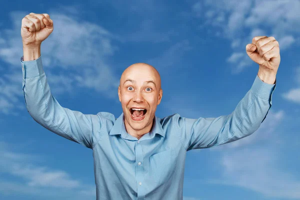 Portrait White bald guy in blue shirt on blue sky background showing thumbs up and smiling