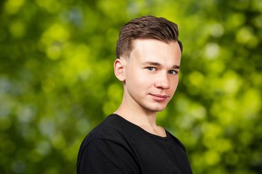 yeşil bokeh arka plan üzerinde kameraya bakarak siyah t-shirt giymiş gülümseyen portre beyaz genç adam modeli