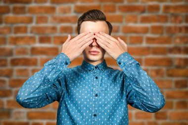 portre Beyaz genç adam mavi gömlek giymiş, gözlerini ellerini kapatır. Tuğla duvar arka plan üzerinde Adam