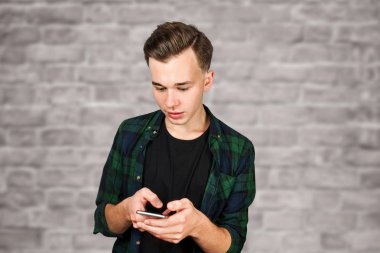 Beyaz genç adam cep telefonuna bir mesaj yazar ve gülümser. Tuğla duvardaki adam