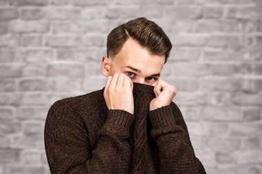 kazak yüzünü gizleme portre Beyaz genç adam. Tuğla duvar arka plan üzerinde Adam