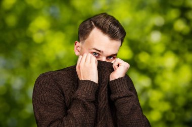 kazak yüzünü gizleme portre Beyaz genç adam. Yeşil bokeh arka plan üzerinde Man