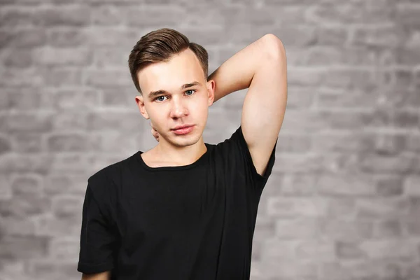 portrait white young guy model dressed in black t-shirt looking at the camera on brick wall background