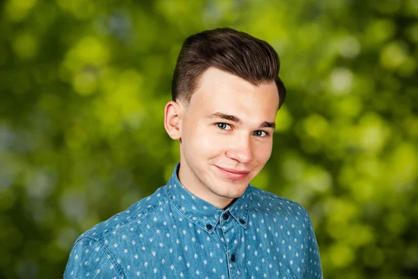 Улыбающийся портрет белый молодой парень модель, одетый в синюю рубашку, глядя на камеру на зеленом фоне боке — стоковое фото