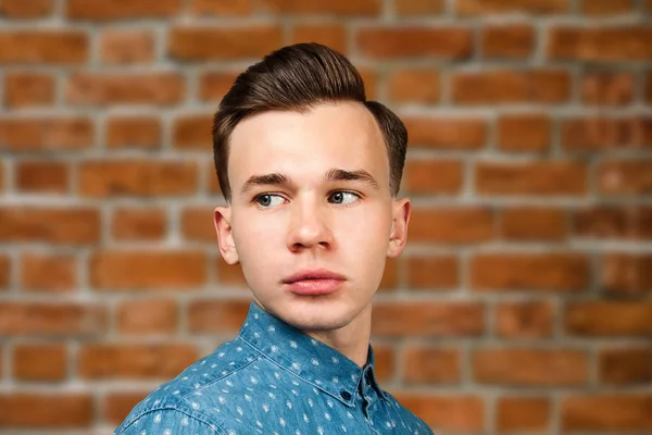 portrait white young guy model dressed in blue shirt looking at the camera on brick wall background