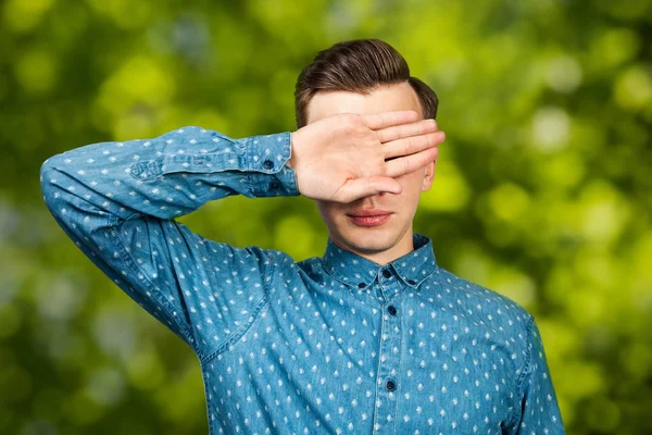 portrait White young man dressed in blue shirt, closes eyes his hands. Man on green bokeh background