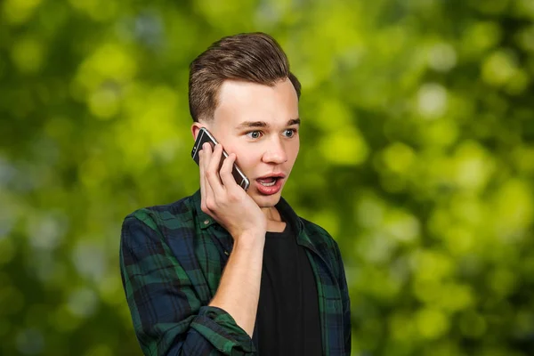Porträtt av rädd vit ung kille skriver ett meddelande på mobiltelefonen och ler. Man på grön bokeh bakgrund — Stockfoto