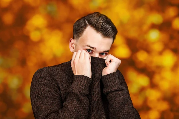 Portré fehér fiatal srác rejtőzik arcát a pulóvert narancssárga, piros őszi háttér — Stock Fotó