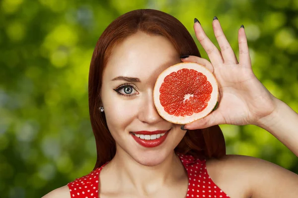 Porträt eines rothaarigen jungen Mädchens, das seinen Mund mit einer halben roten Grapefruit bedeckt — Stockfoto