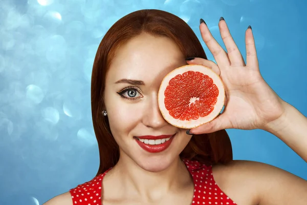 Retrato de uma menina ruiva cobrindo sua boca com meia toranja vermelha — Fotografia de Stock