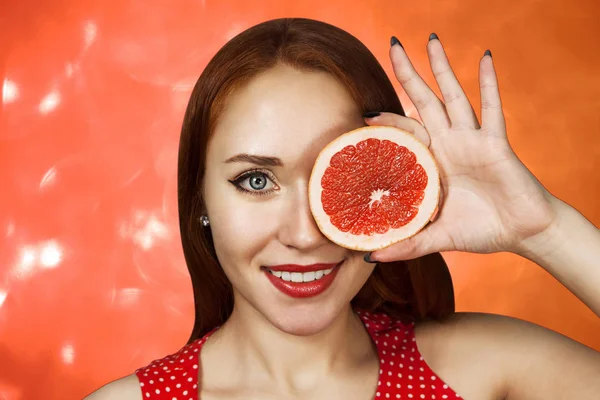 Retrato de uma menina ruiva cobrindo sua boca com meia toranja vermelha — Fotografia de Stock