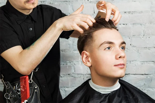 Cabelo de barbeiro styling de cara jovem na barbearia no fundo da parede de tijolo, cabeleireiro faz penteado para um jovem. Penteado Pompadour . — Fotografia de Stock