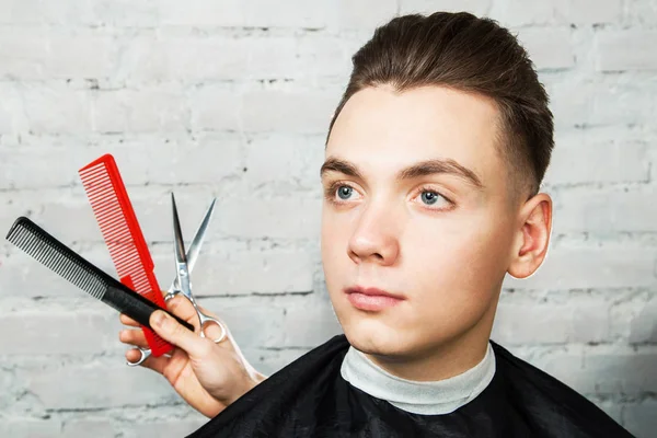 White young man with Pompadour hairstyle in barbershop on a brick wall background with combs and scissors
