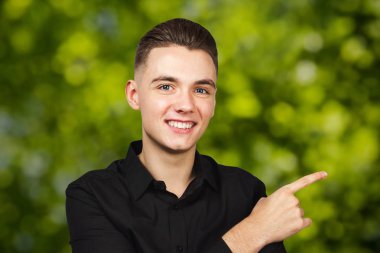 Siyah tişörtlü, yeşil renkli genç adam işaret parmağı ve gülümseme bir yana.