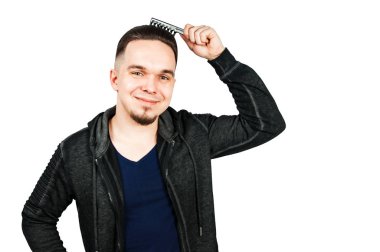 Kapüşonlu genç sakallı adam fotokopi alanının yanında tarak tutuyor. Beyaz arkaplanda izole