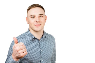 Mavi gömlek giymiş yakışıklı genç adam portresi başparmak gösterir. Beyaz arka planda yalıtılmış