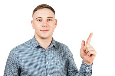 Mavi gömlek giymiş yakışıklı genç adam Portresi işaret parmağı yukarı gösterir ve gülümsüyor. Beyaz arka planda yalıtılmış