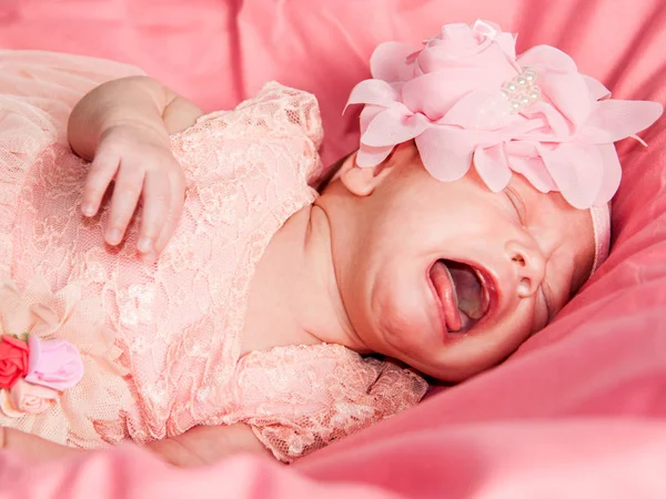 Retrato de cerca de una niña recién nacida vestida con un vestido rosa, con una corona y una flor en la cabeza — Foto de Stock