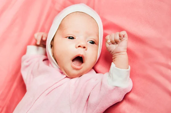 Menina recém-nascida em vestido rosa e coroa de crochê, encontra-se na cama rosa . — Fotografia de Stock
