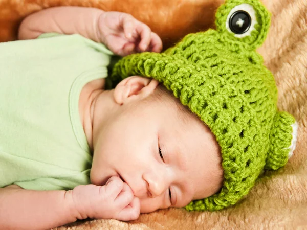 Retrato de un bebé recién nacido durmiendo sobre una tela a cuadros marrón en un sombrero de rana verde . — Foto de Stock