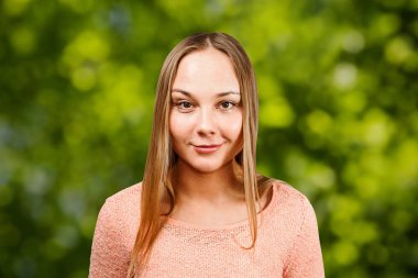 Yeşil bokeh arka plan üzerinde, bej gömlek güzel gülümseyen genç kadının portresi kadar yakın