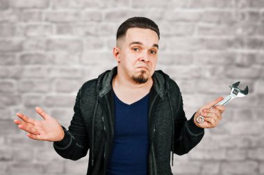 Tuğla duvar arka plan üzerinde ayarlanabilir anahtarı tutan sakallı genç adam portresi
