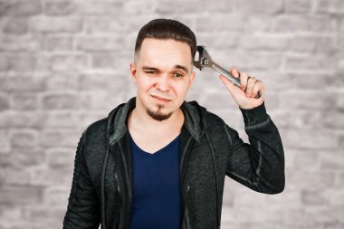 Tuğla duvar arka plan üzerinde ayarlanabilir anahtarı tutan sakallı genç adam portresi