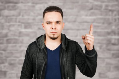 Tuğla duvar arka plan üzerinde yakışıklı yetişkin adam portresi. Sakallı beyaz adam işaret parmağını yukarı gösteriyor.