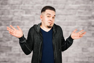 Şaşkın genç sakallı adam silkiyor, tuğla duvar arka plan üzerinde