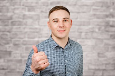 Mavi gömlek giymiş yakışıklı genç adam Portresi tuğla duvar arka plan üzerinde başparmak gösterir