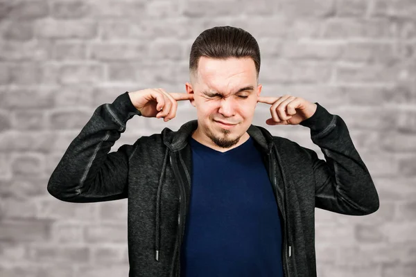 Portrait White man closes the ears in blue shirt on brick wall background — Stock Photo, Image