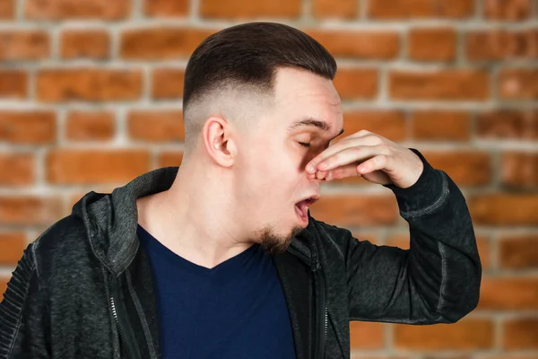 portrait of Caucasian guy, close nose, stinks. Man on brick wall background