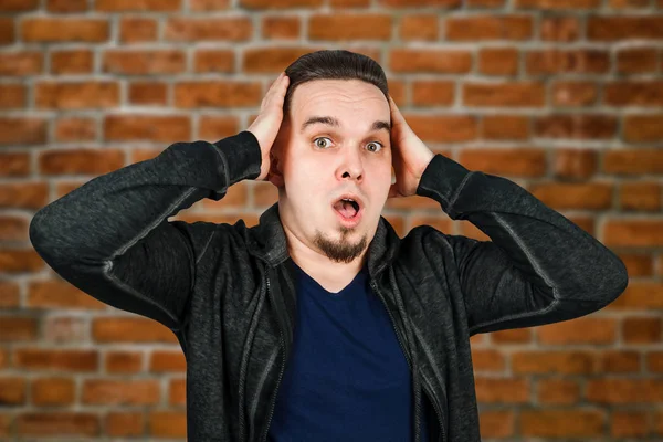 Portrait of young man scared, hold hand head and open mouth. Man on brick wall background — Stock Photo, Image