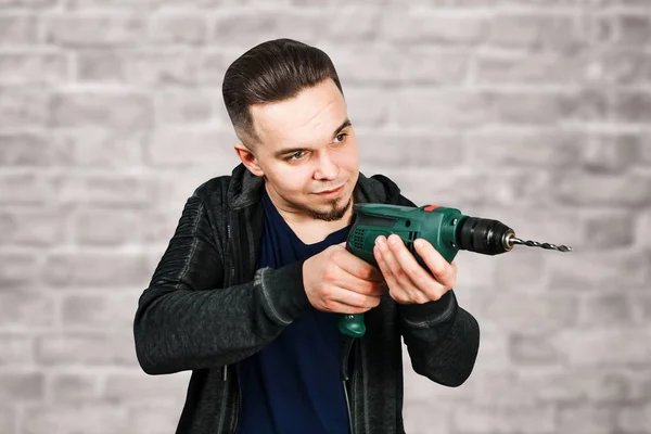 Young bearded guy holding drill on brick wall background — Stock Photo, Image