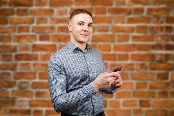 White young guy looking at his smartphone on a brick wall background