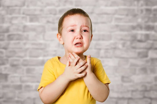 Плаче хлопчик у жовтій футболці, закриває обличчя руками та криками, студія на фоні цегляної стіни — стокове фото