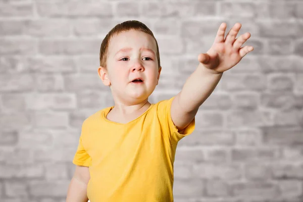 Crying Baby Boy i en gul T-shirt täcker hans ansikte med händer och rop, Studio på tegelvägg bakgrund — Stockfoto