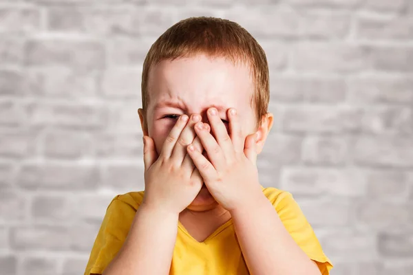 Sarı bir t shirt ağlayan bebek çocuk elleri ve bağırır, tuğla duvar arka plan üzerinde stüdyo ile yüzünü kaplar